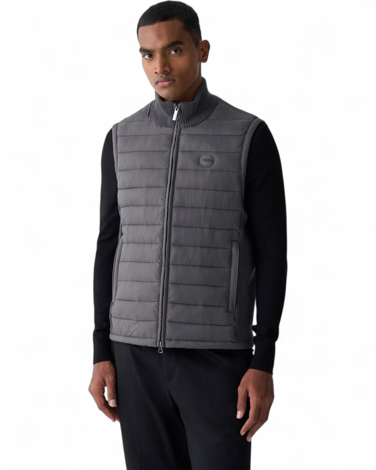 Vista frontale del gilet uomo trapuntato grigio con zip e collo alto, inserti in maglia a costine e logo tono su tono sul petto sinistro.