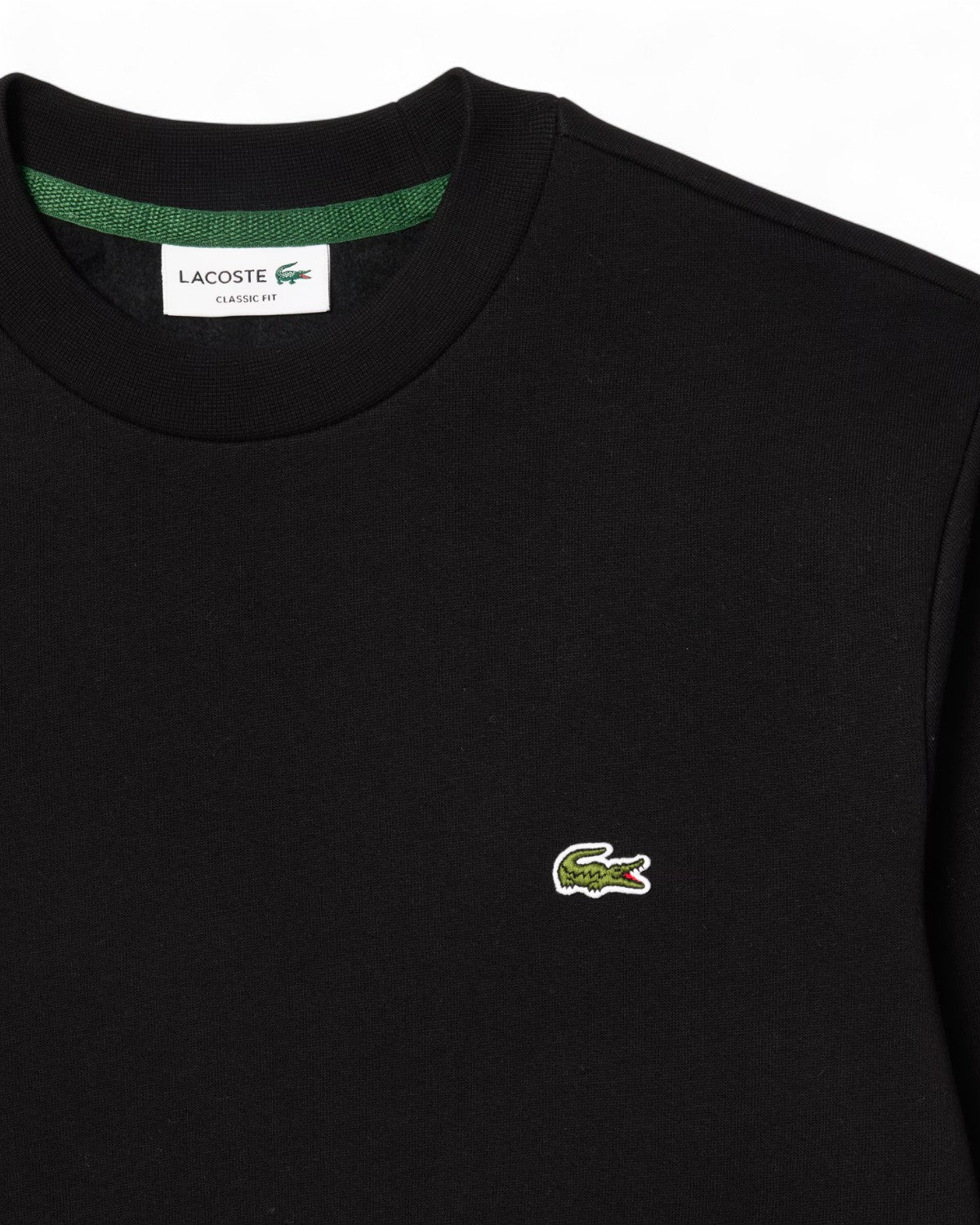 Dettaglio del logo ricamato Lacoste su felpa girocollo in pile nera, realizzata in cotone organico per un comfort invernale.