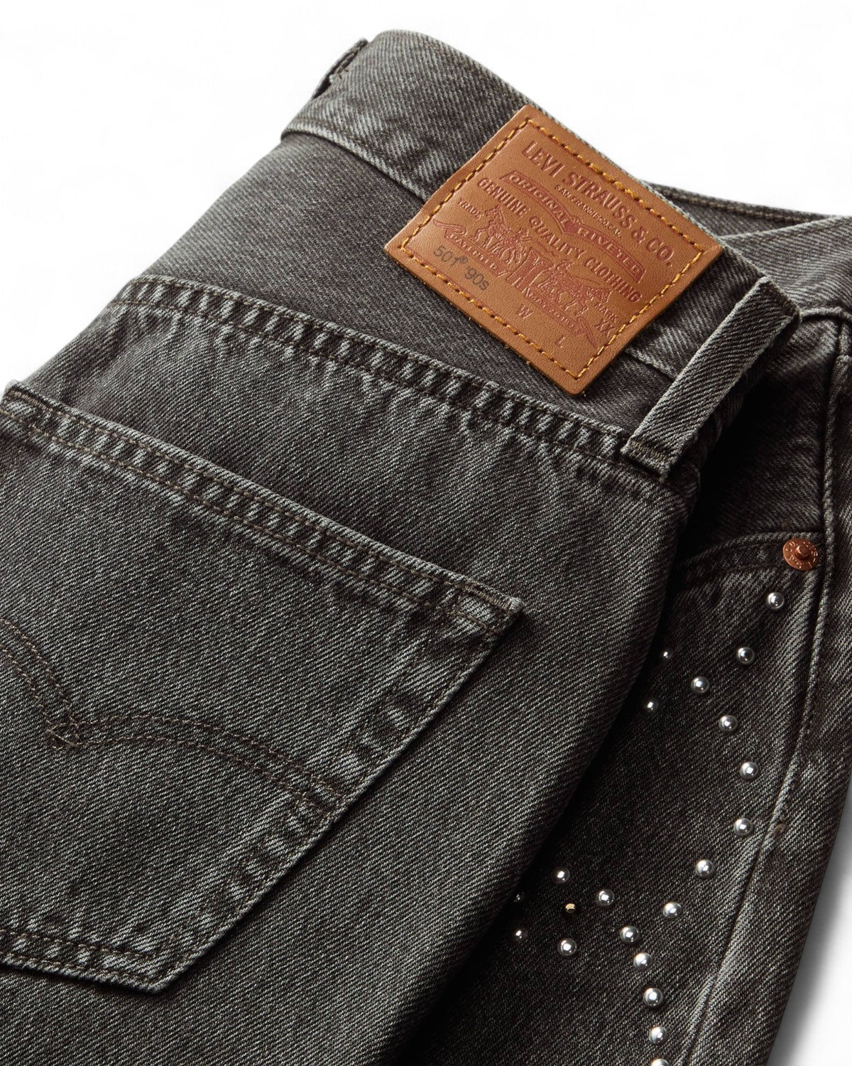 Dettaglio del denim nero dei jeans Levi's 501 Anni '90 con patch in pelle e borchie laterali, design resistente e iconico.