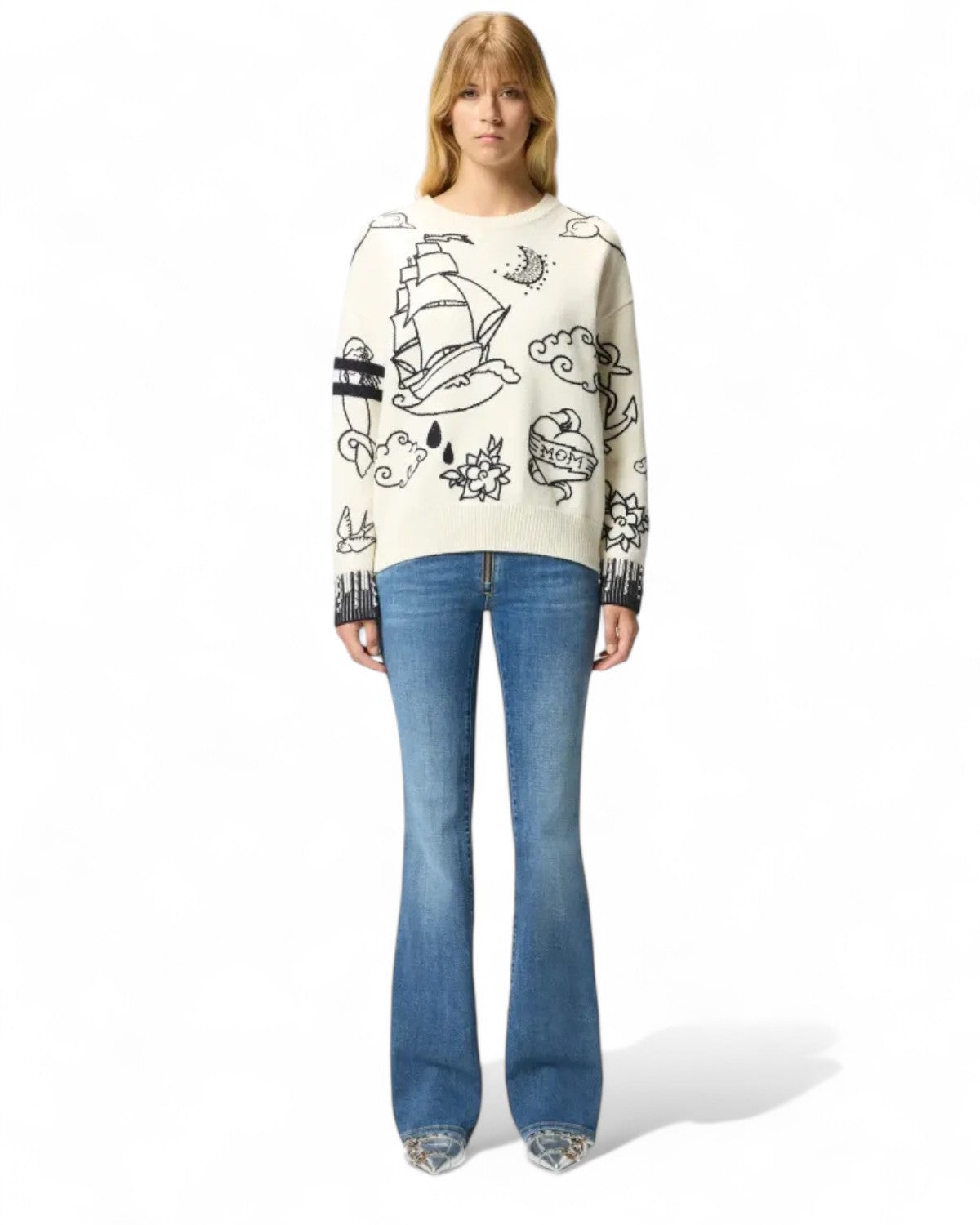 Modella indossa maglione PINKO in lana merino con fantasie tattoo e strass, abbinato a jeans a zampa per outfit casual elegante.