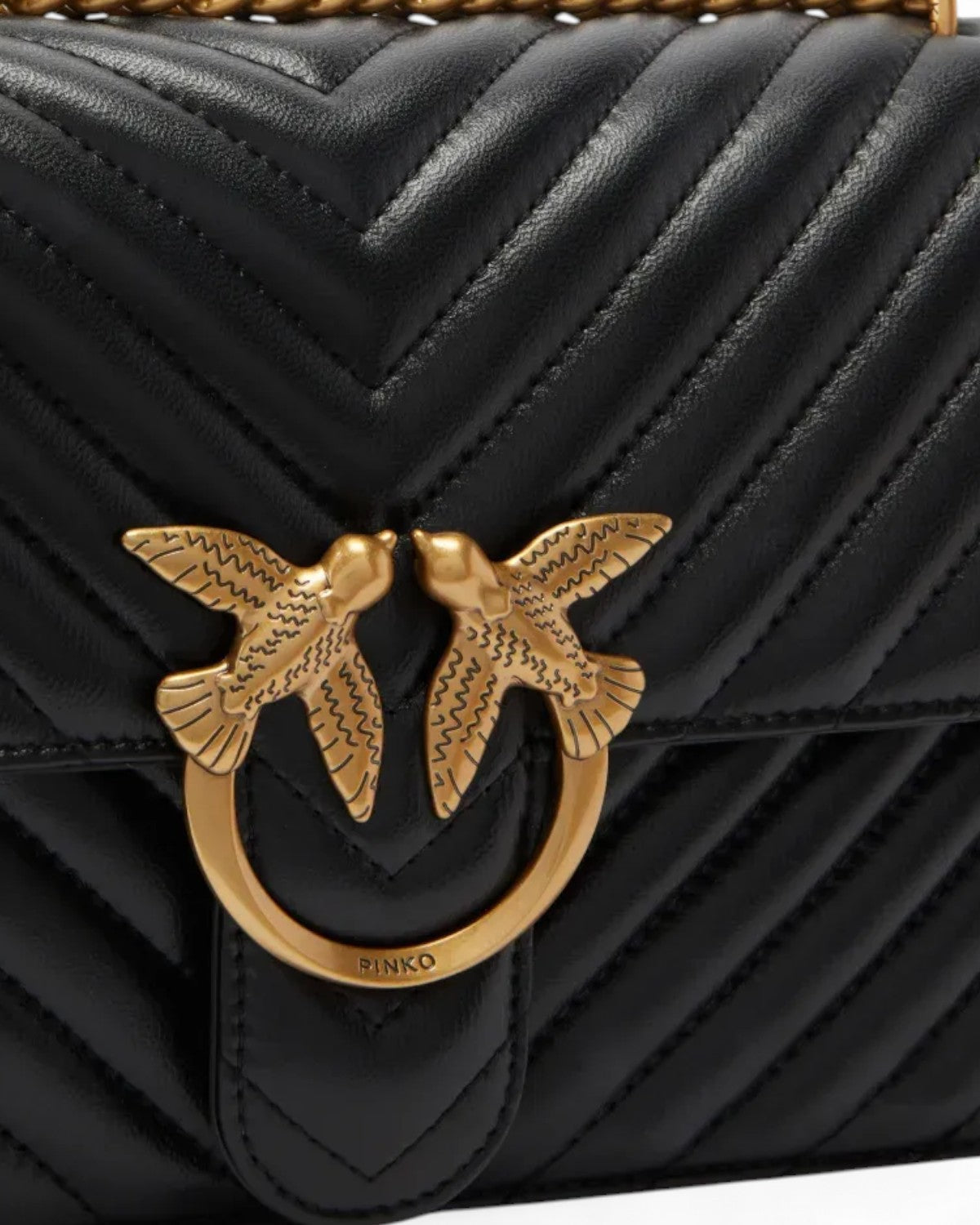 Dettaglio della fibbia Love Birds dorata sulla Love Bag Nappa Chevron con Tracolla - Pinko, su pelle nera matelassé a motivo chevron.