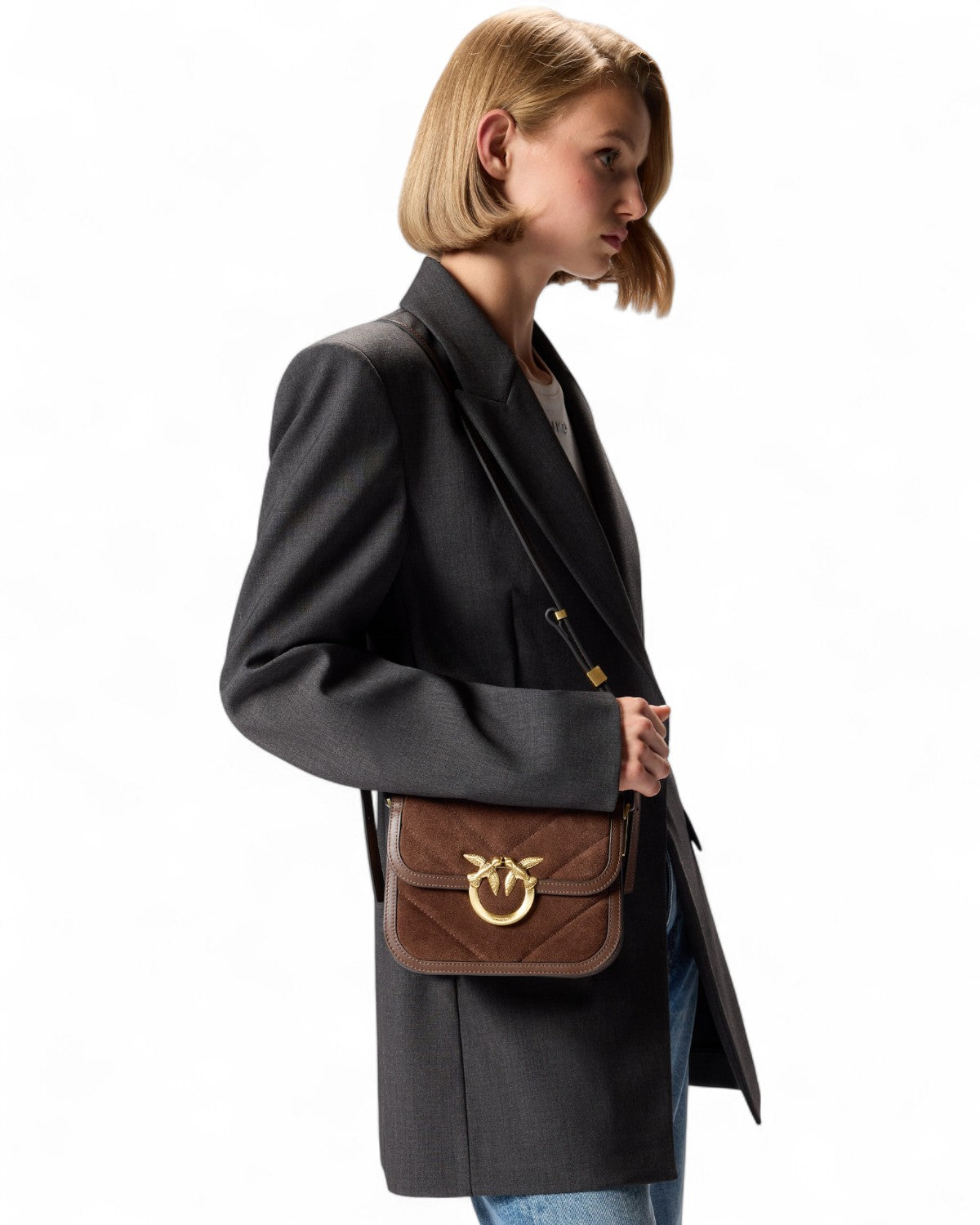 Modella indossa la PINKO Mini Love Bag Box marrone a tracolla, abbinata a blazer grigio e jeans, perfetta per look invernali donna FW26.